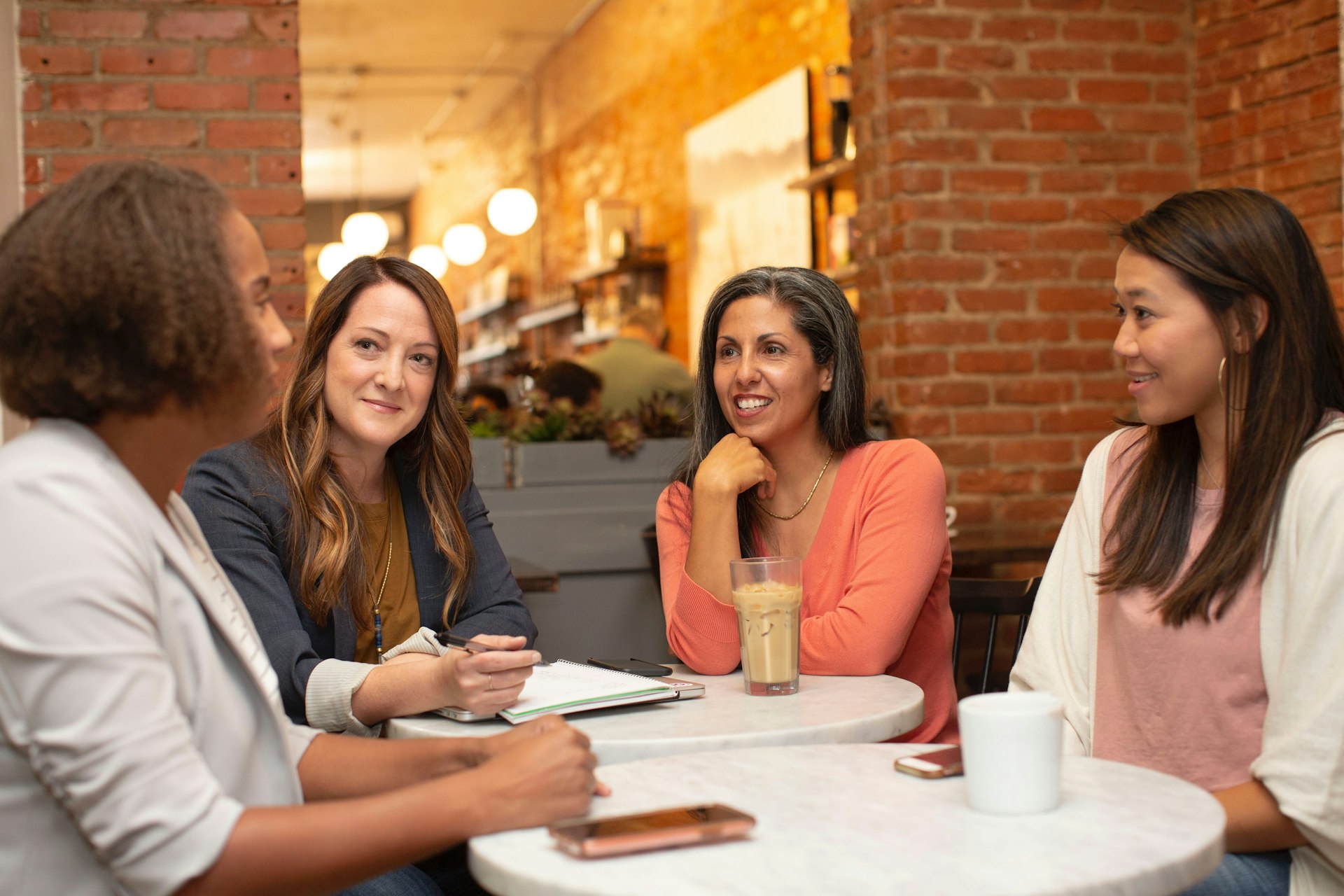 Quatre femmes souriantes discutent autour d’une table de café pour choisir un consultant IA
